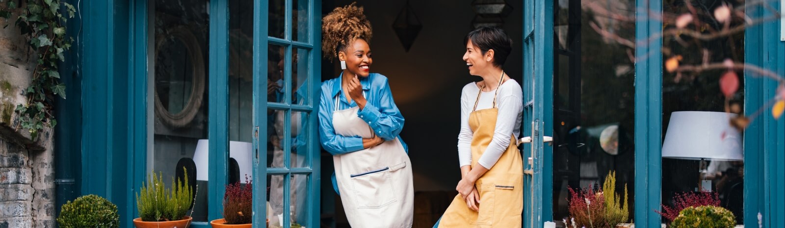 two workers in aprons standing in the doorway of a shop