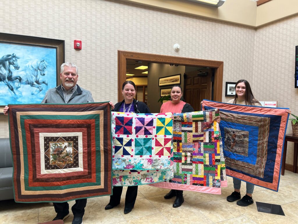 Dave displaying quilts with members of Family Crisis Shelter