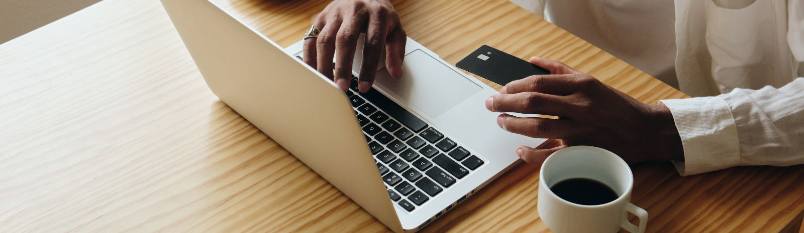 Person using bank card at laptop computer while have a cup of coffee.