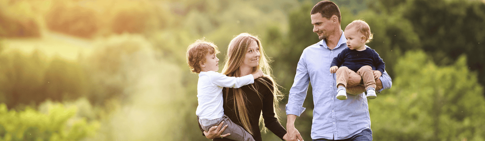 Nuclear family walking among lush green landscape with parents carrying children.